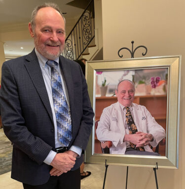 Doctor in a suit standing beside a framed portrait of himself