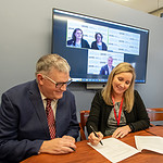 Susan Long, right, signs the Memorandum of Understanding as Nathan Johnson, left, and officials of Western Piedmont Community College, onscreen, look on.