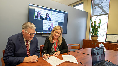 Susan Long, right, signs the Memorandum of Understanding as Nathan Johnson, left, and officials of Western Piedmont Community College, onscreen, look on.