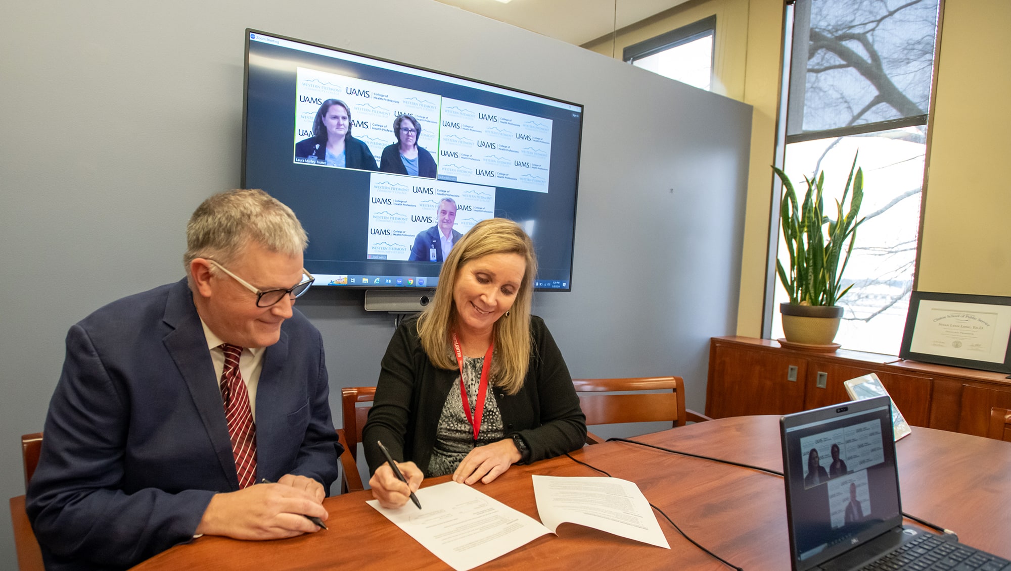 Susan Long, right, signs the Memorandum of Understanding as Nathan Johnson, left, and officials of Western Piedmont Community College, onscreen, look on.