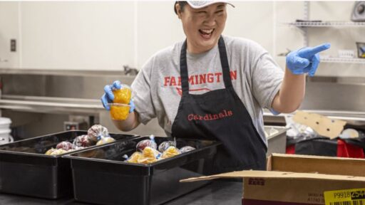 A lunchroom kitchen worker in Farmington smiles and laughs while unpacking food.