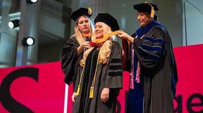 A graduate dons her hood during the UAMS College of Nursing’s hooding and pinning ceremony.