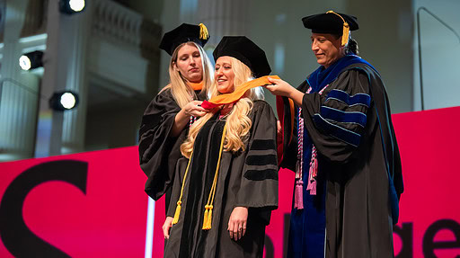 A graduate dons her hood during the UAMS College of Nursing’s hooding and pinning ceremony.