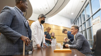 Johnathan Goree, M.D., left, who directs Interventional Pain Management Services at UAMS, and Rohit Dhall, M.D. , chair of the UAMS College of Medicine Department of Neurology, talk with Keefe while he signs copies of his books after the lecture.