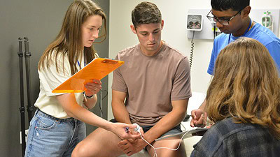 Group of high school students in a clinical patient room check pulse rate of another student