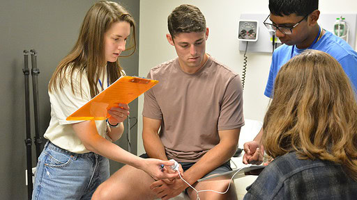 Group of high school students in a clinical patient room check pulse rate of another student