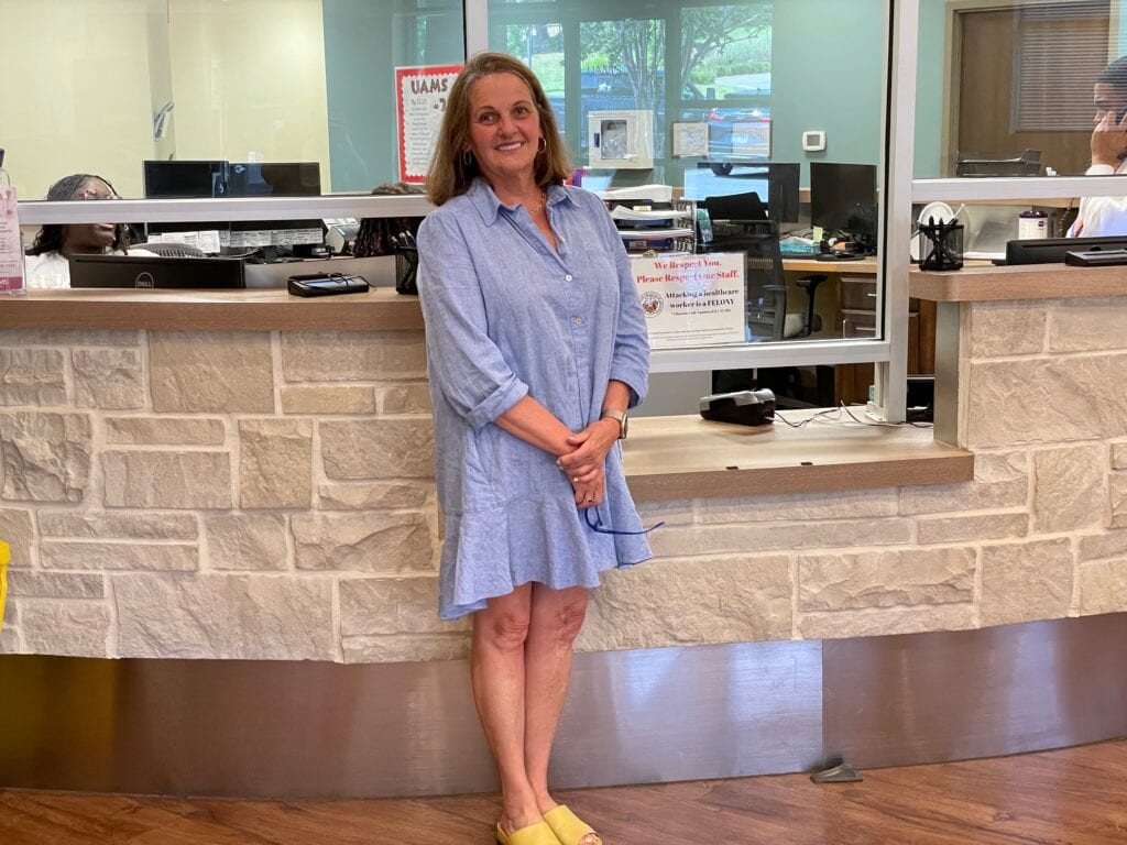 Lea Bannister, M.D., arrives as a patient for a follow-up visit with David Bumpass, M.D., an UAMS orthopaedic spine surgeon, at a UAMS orthopaedic clinic in Little Rock. Bannister stands at check-in counter in blue dress