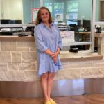 Lea Bannister, M.D., arrives as a patient for a follow-up visit with David Bumpass, M.D., an UAMS orthopaedic spine surgeon, at a UAMS orthopaedic clinic in Little Rock. Bannister stands at check-in counter in blue dress