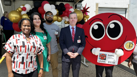 At the back of the Monroe Building and the entryway to the Stocked & Reddie Food Pantry, Katriel Alexander, left, Jennifer Mondragon, Christopher Guinn, Chancellor Cam Patterson and UAMS mascot Reddie celebrate the 5th anniversary of the establishment of the pantry.