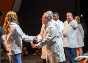 A new medical student shakes hands with Dean Steven Webber, M.D., after receiving her white coat.