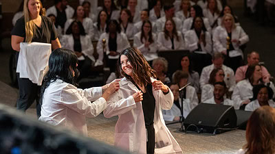 A student dons her white coat during the College of Nursing ceremony.