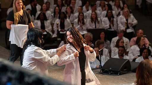 A student dons her white coat during the College of Nursing ceremony.