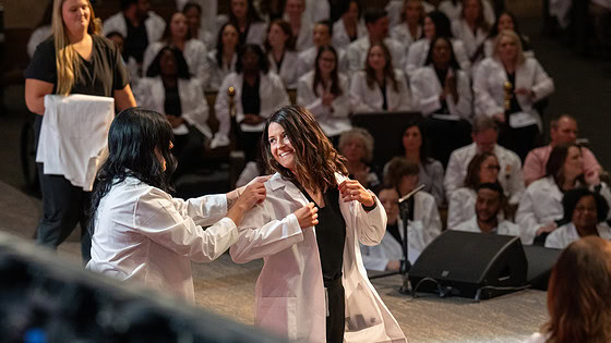 A student dons her white coat during the College of Nursing ceremony.