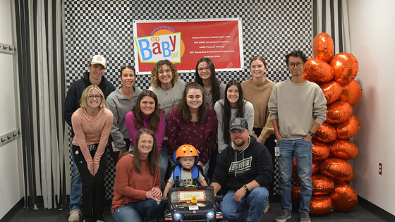 Students and faculty present a GoBabyGo modified ride-on care to a child with mobility issues.