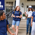 A diverse group of smiling young people talk as they exit a building and walk down stairs.