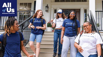 A diverse group of smiling young people talk as they exit a building and walk down stairs.