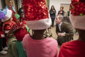 A close-up view from behind the carolers and their sparkly hats as they talk with Chancellor Cam Patterson, M.D., MBA.