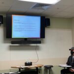 Matthew Boone, LCSW, sits in front of a group of faculty members near a screen that reiterates points about helping students in difficulty.
