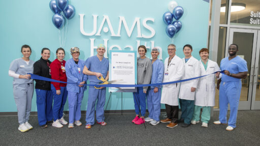 A group photo in front of urology clinic with Brian Langford, M.D., holding large scissors, about to cut a ribbon in front of them all.