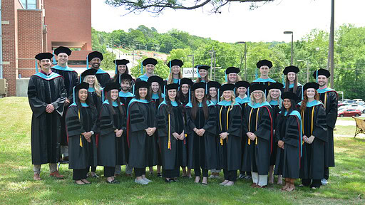 The UAMS Physical Therapy Class of 2025 poses in their caps and gowns on the lawn of the UAMS Northwest Regional Campus in Fayetteville.