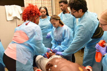 HCOP Academy scholars, including Amilah Hall (center), and UAMS Simulation Center instructors apply a tourniquet to a manikin during a trauma-care demonstration. 