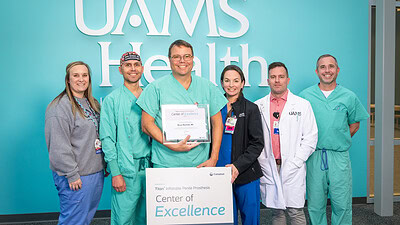 Bruno Machado, M.D., is surrounded by others at the UAMS Urology Clinic as he displays the Center of Excellence plaque.