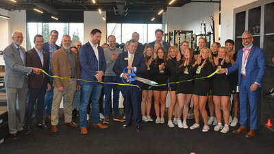 Dr. Lowry Barnes cuts the ribbon at the new UAMS orthopaedics and sports medicine clinic in Bentonville, as clinic staff and providers, Bentonville community leaders, the Bentonville High School cheer squad look on and applaud.