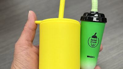 Photo of a hand holding vaping devices shaped like boba tea cups and sippy cups