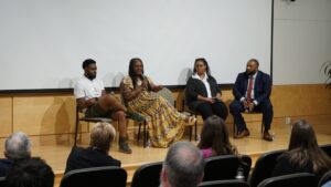 A group of five people are seated in chairs on a stage.