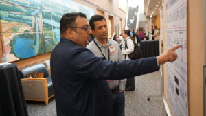 A man points at a research poster while another man stands next to him.
