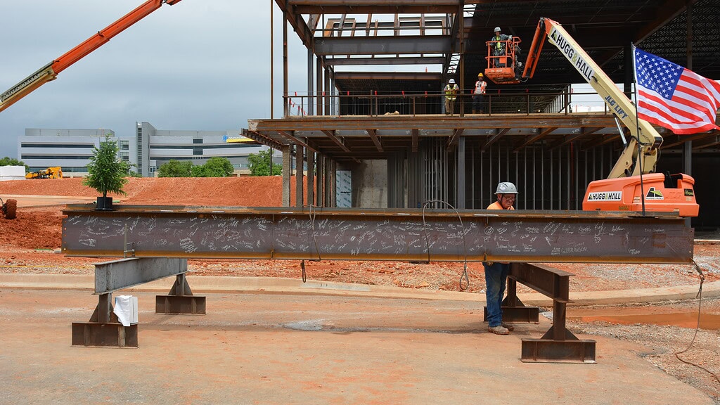 A metal i-beam, signed by attendees at the topping out ceremony for the UAMS Health Orthopaedics & Sports Medicine Hospital in Springdale, is ready to be hoisted in place by a crane.