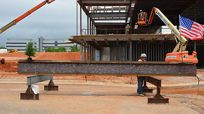 A metal i-beam, signed by attendees at the topping out ceremony for the UAMS Health Orthopaedics & Sports Medicine Hospital in Springdale, is ready to be hoisted in place by a crane.