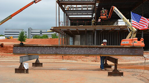 A metal i-beam, signed by attendees at the topping out ceremony for the UAMS Health Orthopaedics & Sports Medicine Hospital in Springdale, is ready to be hoisted in place by a crane.
