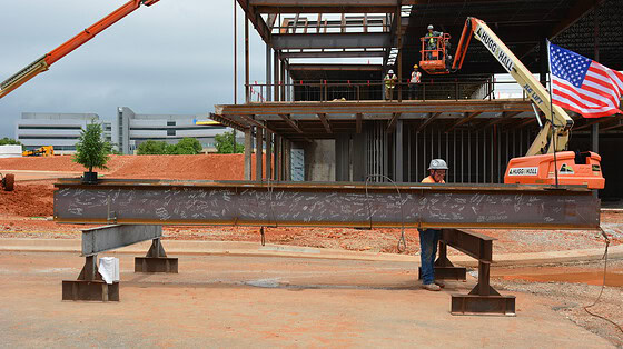 A metal i-beam, signed by attendees at the topping out ceremony for the UAMS Health Orthopaedics & Sports Medicine Hospital in Springdale, is ready to be hoisted in place by a crane.