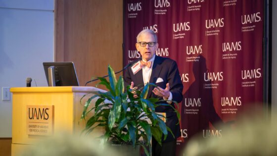Barry Coller is a white man in a suit and bowtie talking behind a podium.