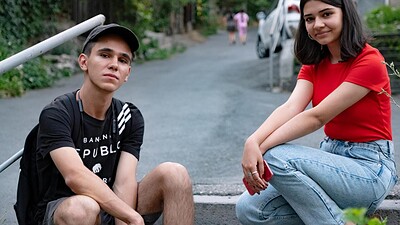 Two teens sitting on a rural road and looking at the camera