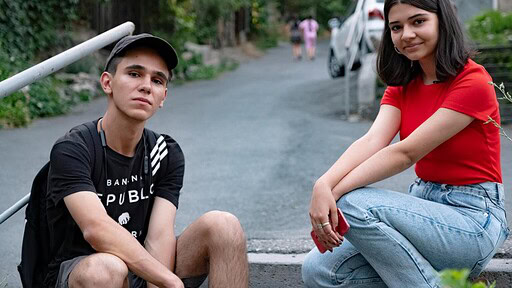 Two teens sitting on a rural road and looking at the camera