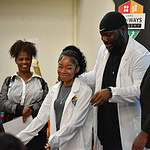 Davonte Hokes, a Hall High and UAMS alumnus and lead pharmacist for Kroger Health, helps a student don her white coat during a ceremony to honor those who took part in the UAMS career development program.