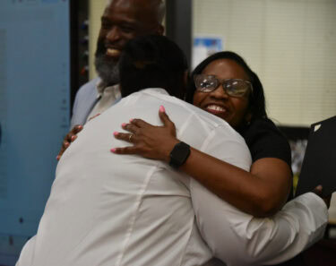 Khi Weston (front) embraces Hall High educator Lawanna Harris as Little Rock School District Superintendent Jermall Wright looks on.