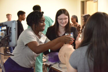 Maddison Guess (center), a 10th grader at Cabot High School, practices on a manikin after learning how to intubate patients during the conference at UAMS.