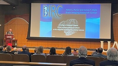Lee Archer at the podium in front of audience with large image of documents describing neurology research