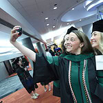 Two graduates pause in caps, gowns and doctoral hoods for a selfie after the ceremony.