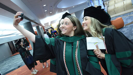 Two graduates pause in caps, gowns and doctoral hoods for a selfie after the ceremony.