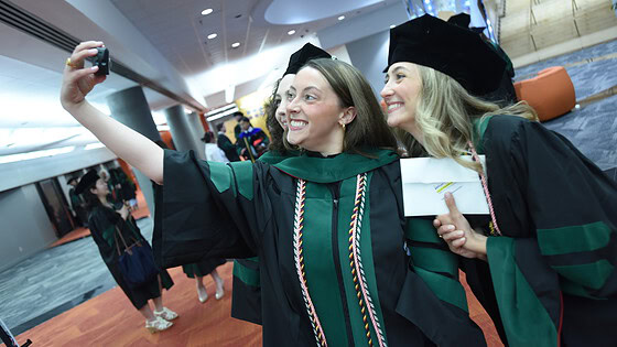 Two graduates pause in caps, gowns and doctoral hoods for a selfie after the ceremony.