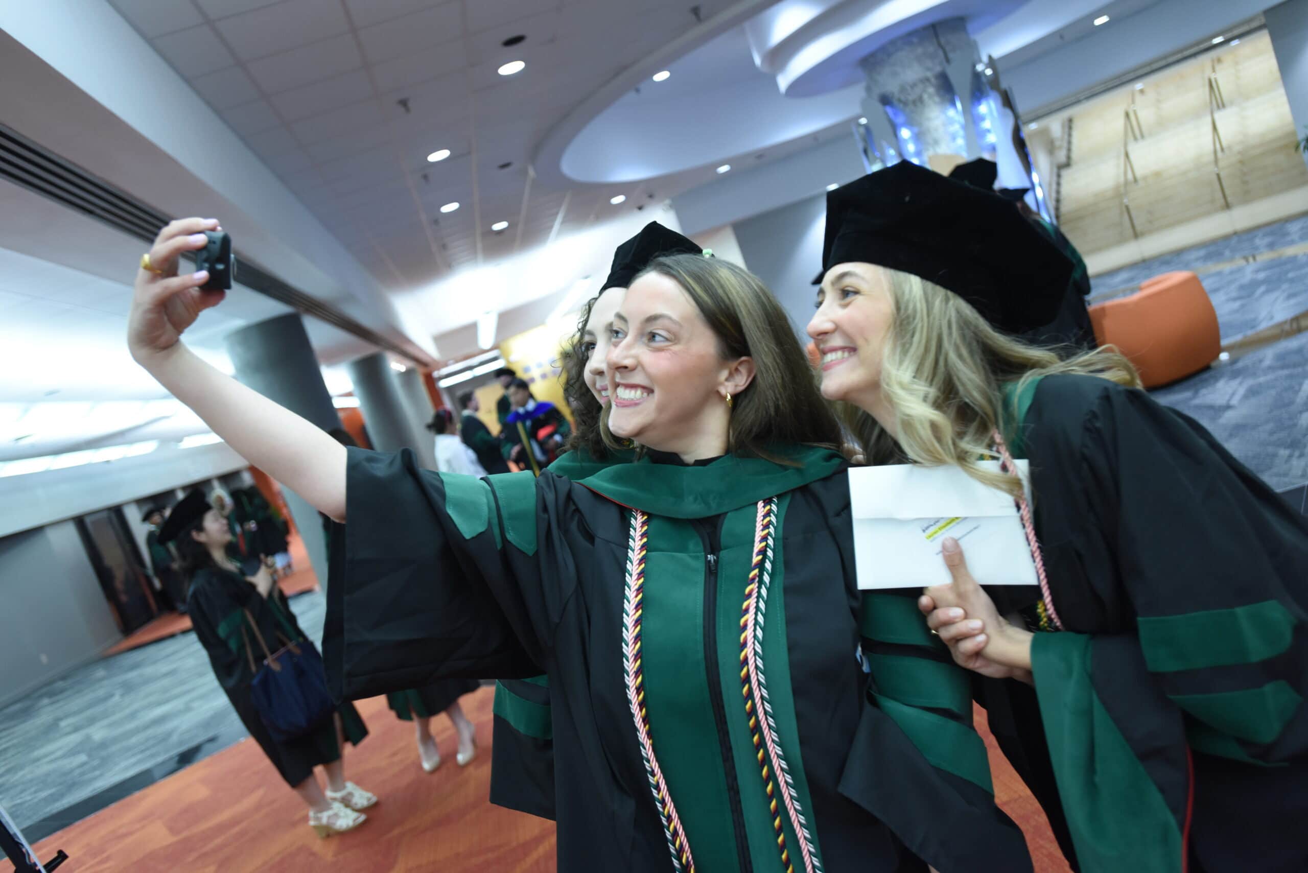 Two graduates pause in caps, gowns and doctoral hoods for a selfie after the ceremony.