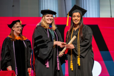 Sarah Rhoads, dean of the College of Nursing, greets one of the graduates onstage as Teresa Whited, the college’s associate dean of academic programs, looks on.