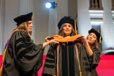 Two faculty members help a graduate don her hood during the College of Nursing ceremony.