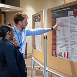 Resident explains research poster to attendee.