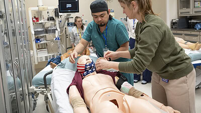 Emergency medicine residents work on a mannikin in a simulation. The mannikin is in a hospital bed in a simulated emergency.