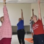 Sarah Rhoads, dean of the UAMS College of Nursing, and four other participants stretch their arms toward the ceiling during the yoga session.